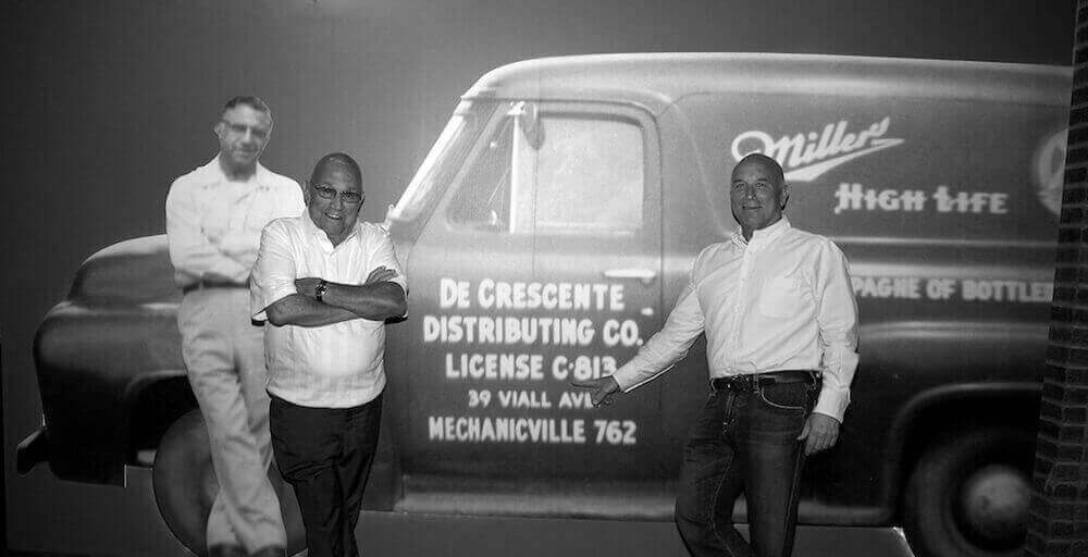 Carmine Sr and CJ in front of an enlarged photo of a Miller High Life truck